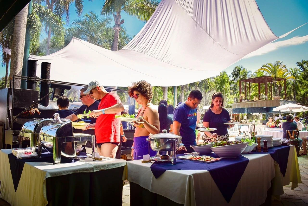 Buffet montado ao ar livre, com equipe em atendimento e convidados no evento
